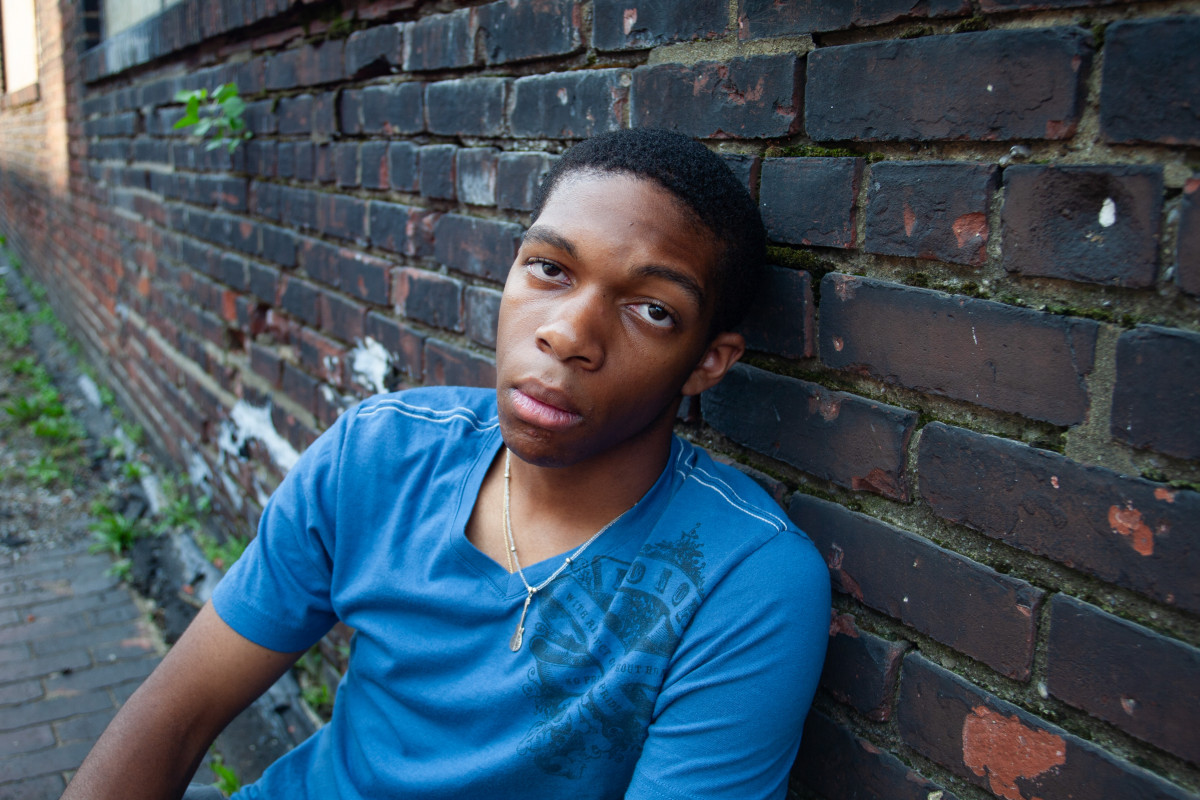 boy sitting against a brick wall