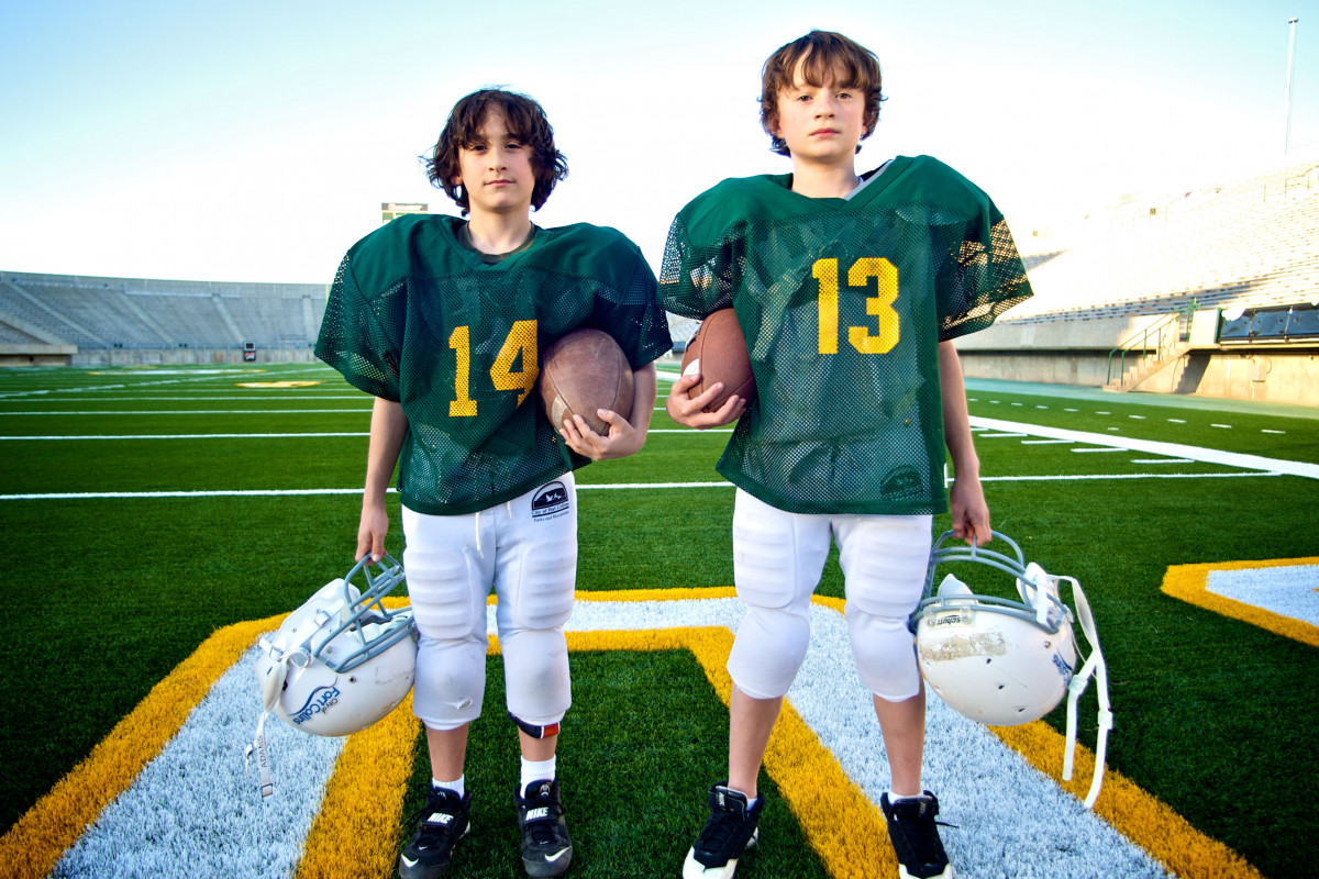 two boys in football gear pose on football field